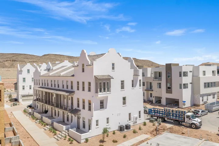 White stucco exterior with tiered gables, multi-story windows, upper-level balcony, and ground-floor patios