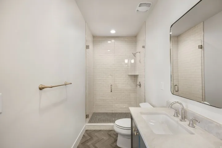 Glass-enclosed shower with subway tile surround, chevron-patterned flooring, single vanity with integrated sink, and a framed mirror