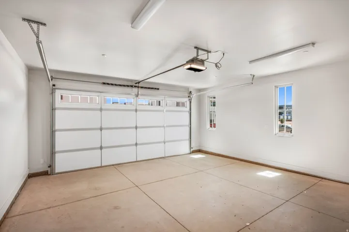 Attached garage with a sectional overhead door featuring upper window panels, concrete flooring, two flush-mount ceiling lights, and two rectangular windows