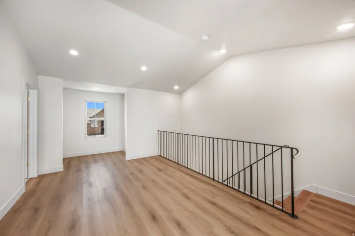 Spacious loft area featuring wood-finish flooring, recessed lighting, a window, and a black metal railing