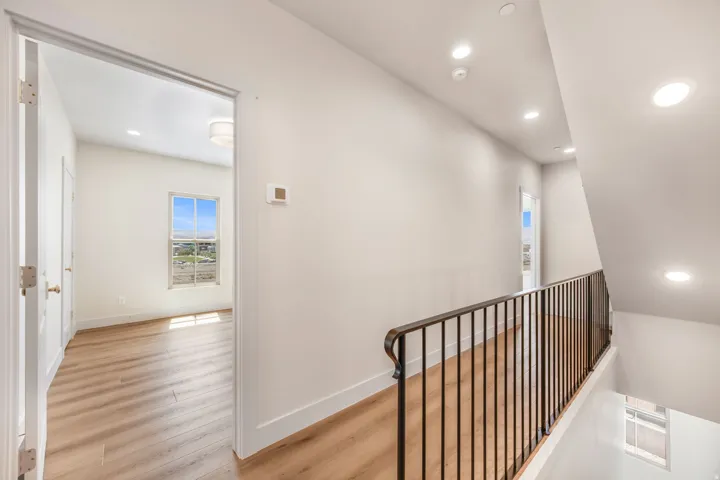 Hallway featuring recessed lighting, wood-finish flooring, a wrought iron railing, and a thermostat
