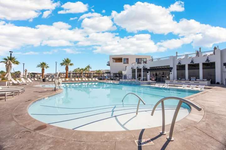 Expansive swimming pool with concrete decking, surrounding lounge areas, mature palm trees, and a building featuring multiple shaded outdoor seating areas
