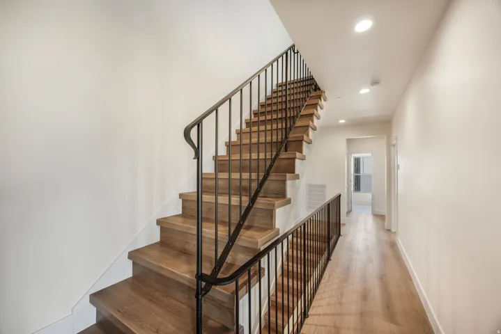 Hardwood staircase with wrought iron railing, complemented by wood-finish flooring and recessed lighting