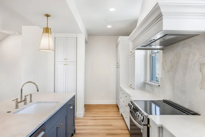Kitchen featuring an integrated sink, polished chrome faucet, white cabinetry, wood-finish flooring, and a built-in range