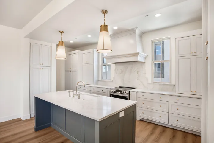 Gourmet kitchen featuring a central island with an undermount sink, pendant lighting, white cabinetry, and wood-finish flooring