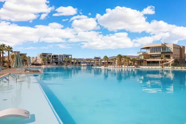 Expansive lagoon-style pool with integrated loungers, surrounded by mature palm trees and contemporary residential buildings
