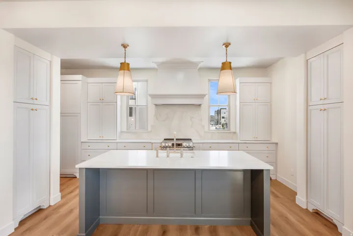 Spacious kitchen featuring an expansive center island, extensive cabinetry with gold-tone hardware, a decorative range hood, and wood-finish flooring