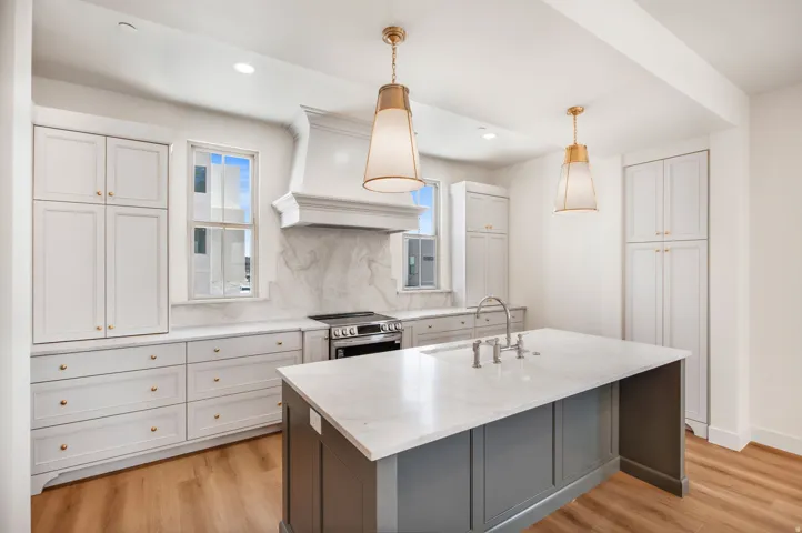 Kitchen featuring white shaker cabinetry, an expansive center island with a sink, elegant pendant lighting, a built-in range with a custom hood, and wood-finish flooring