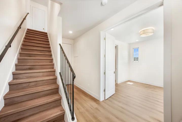 Wood-finish flooring, staircase with dark metal baluster, white interior walls, recessed lighting, and a drum-style ceiling fixture