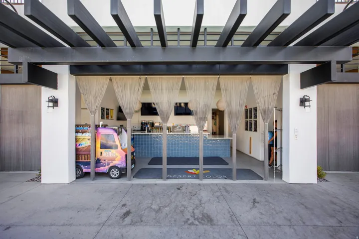 Outdoor lounge area featuring a dark pergola, white columns, textured wall panels, and metal screen dividers