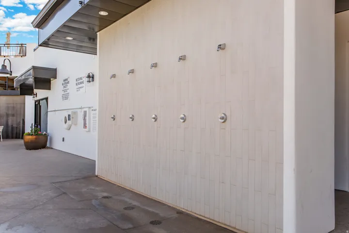 Outdoor shower wall with multiple shower heads, textured tile finish, and concrete flooring