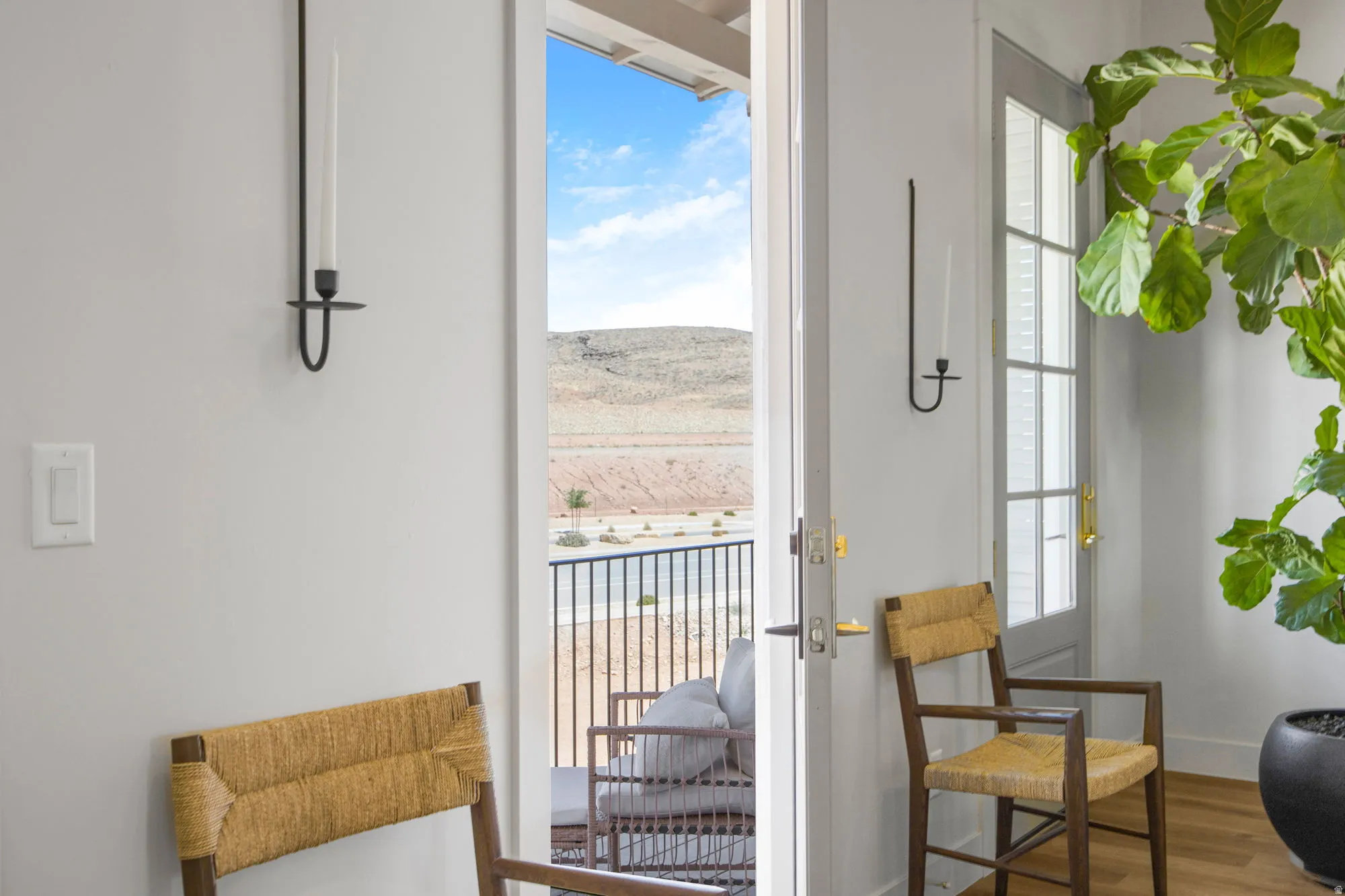 Exterior balcony access with desert scenery, featuring a painted door with window panes, and wall-mounted candle sconces