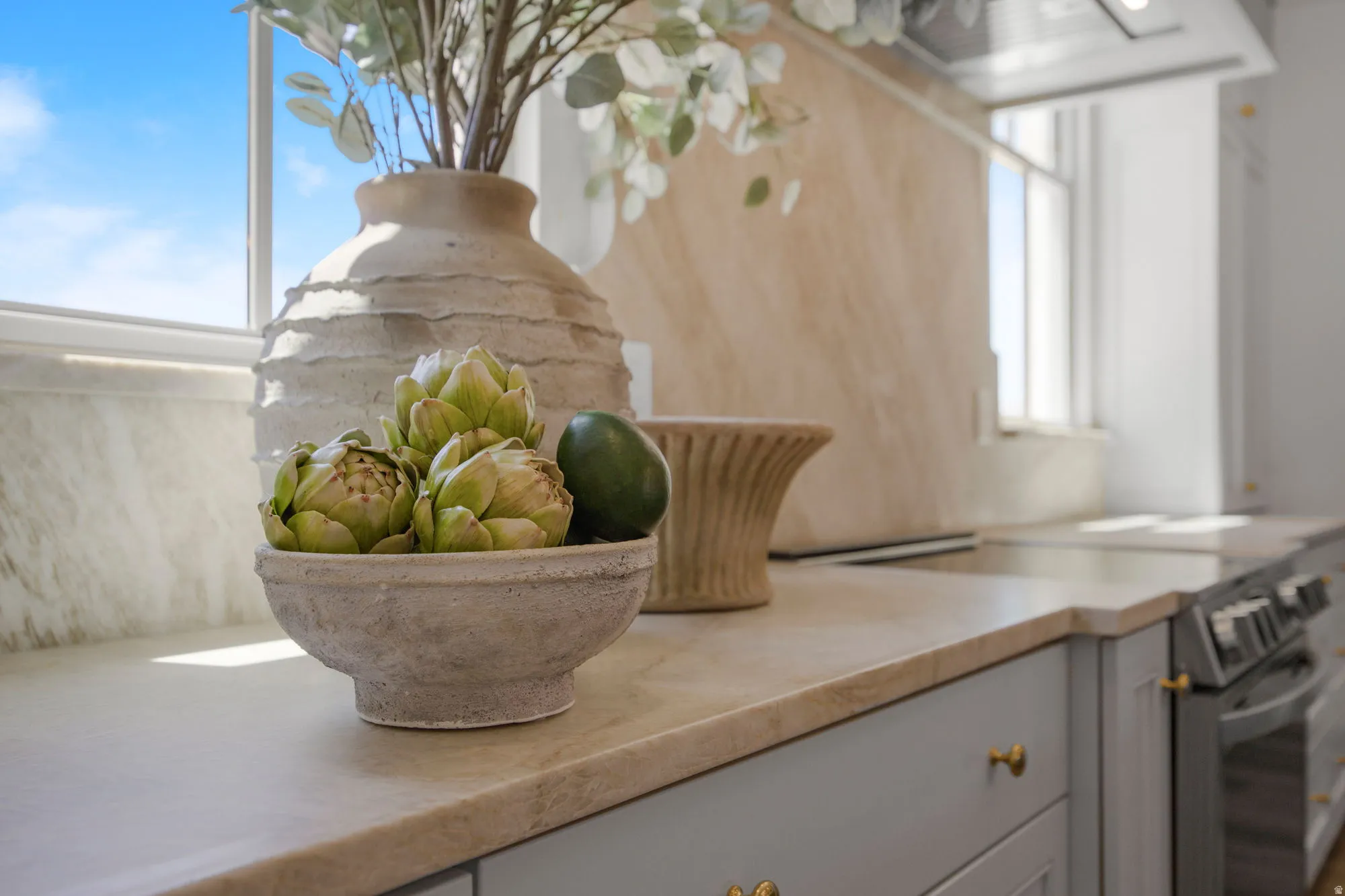 Countertop with integrated backsplash, light-toned cabinetry with brass hardware, and stainless steel range