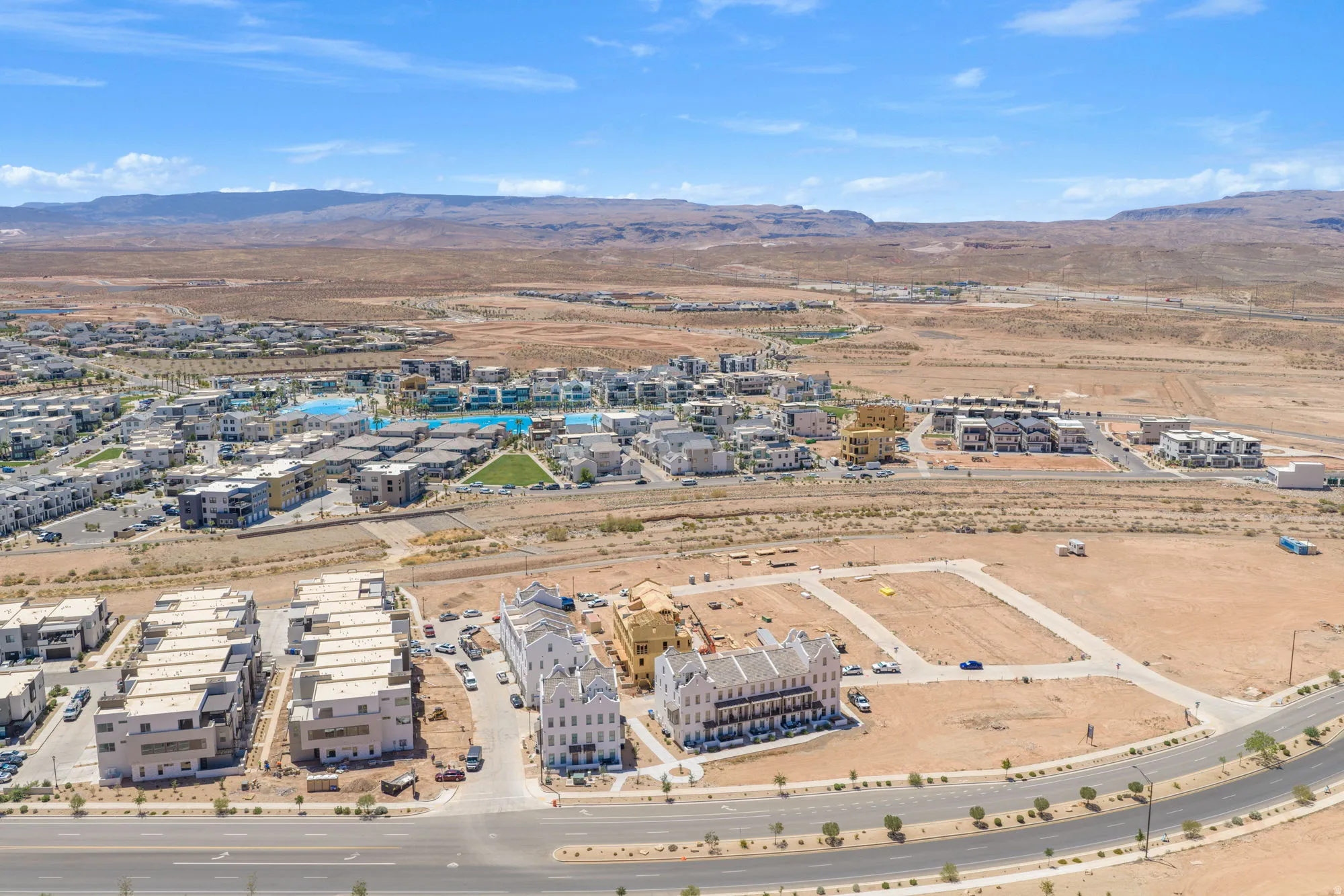 Expansive desert development featuring residential structures, paved roads, and a prominent aquatic amenity