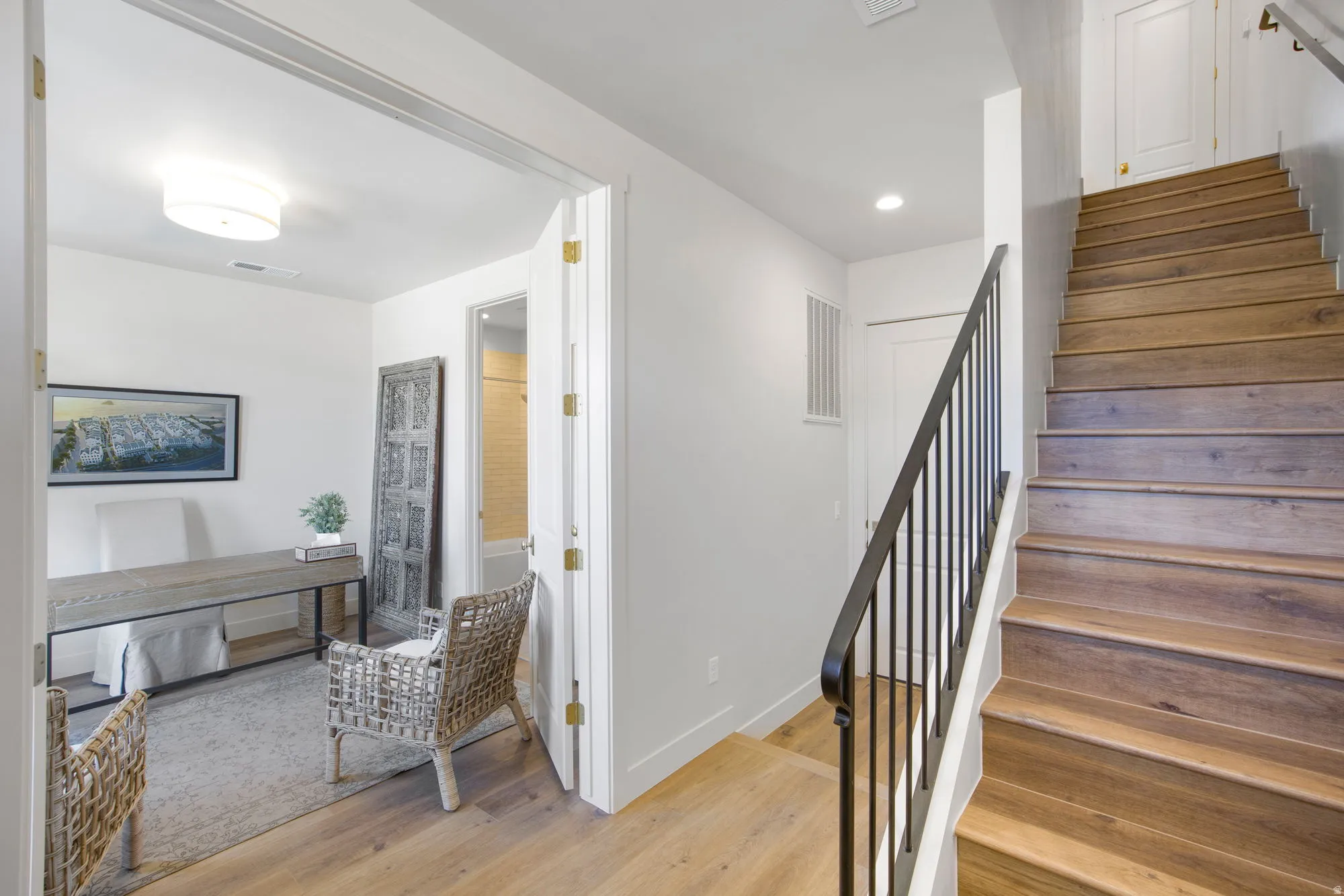 Wood-finish flooring throughout, featuring a staircase with black metal balusters and a wide doorway opening to an additional room