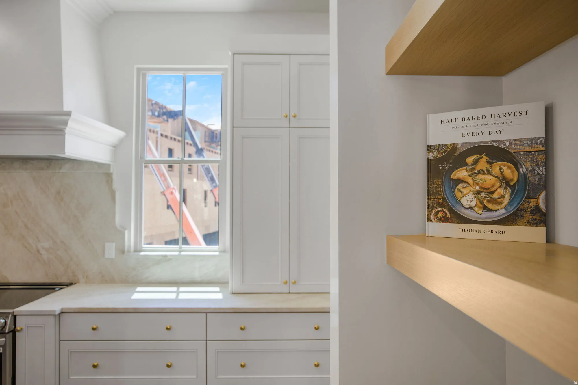 White cabinetry with gold-tone hardware, light-toned stone countertops, and a matching stone backsplash