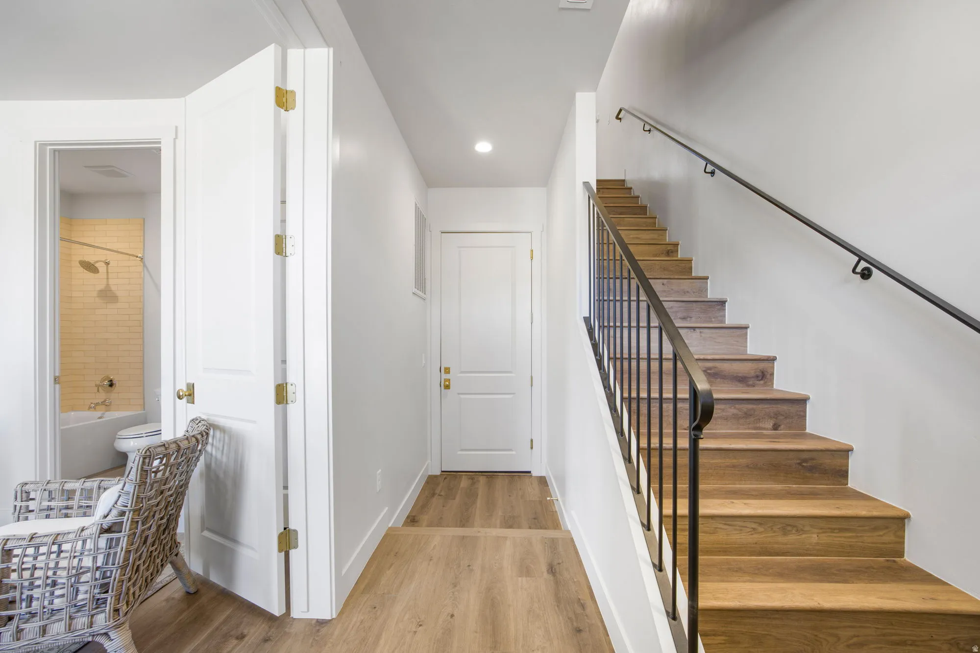 Wood-finish flooring, staircase with wrought iron railing, and recessed lighting