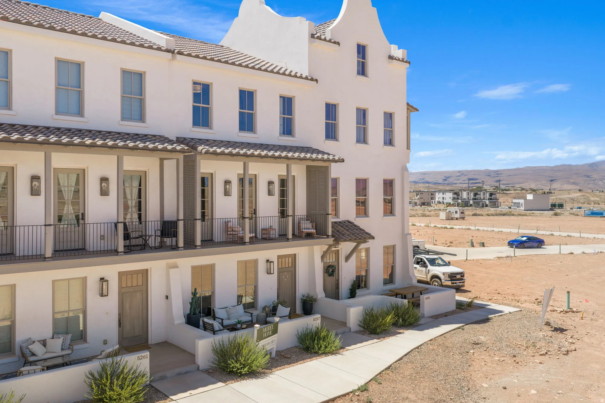 Multi-level stucco exterior with individual balconies featuring black iron railings, and individual ground-level patios