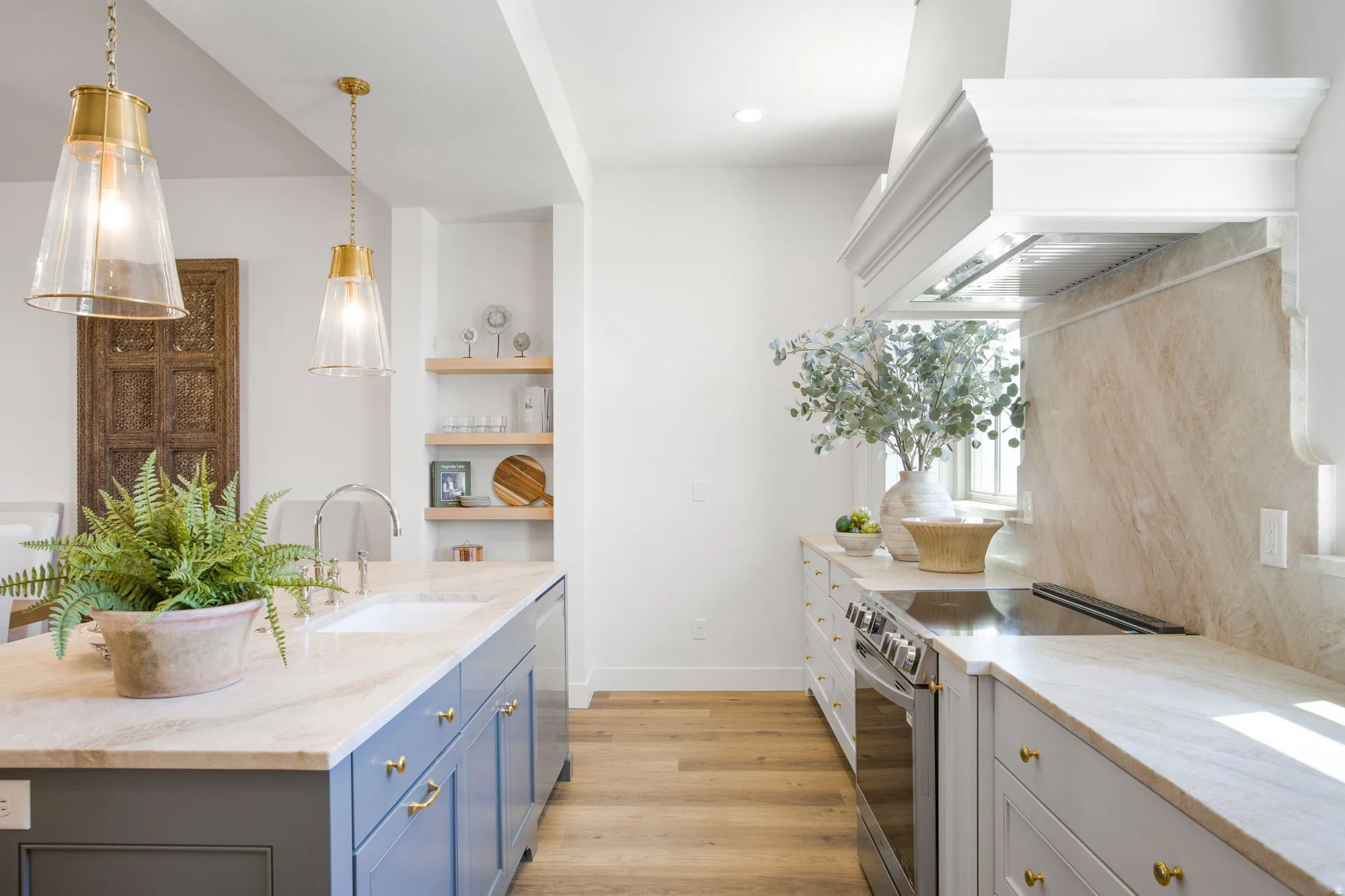 Kitchen featuring an island with an integrated sink, dual pendant lighting, light wood-finish flooring, and open shelving