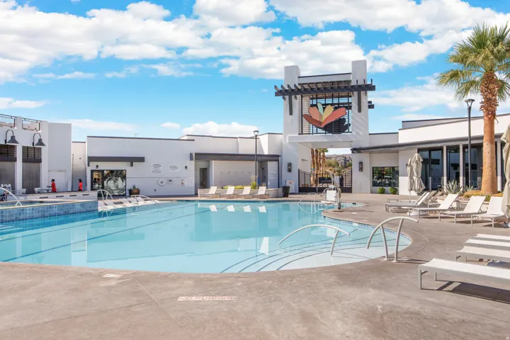Expansive outdoor pool with integrated spa, surrounded by a concrete deck and a modern building featuring large windows and an exterior architectural art piece