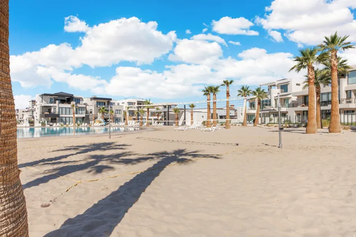 Expansive sand area featuring a volleyball court, mature palm trees, and a pool surrounded by lounge chairs