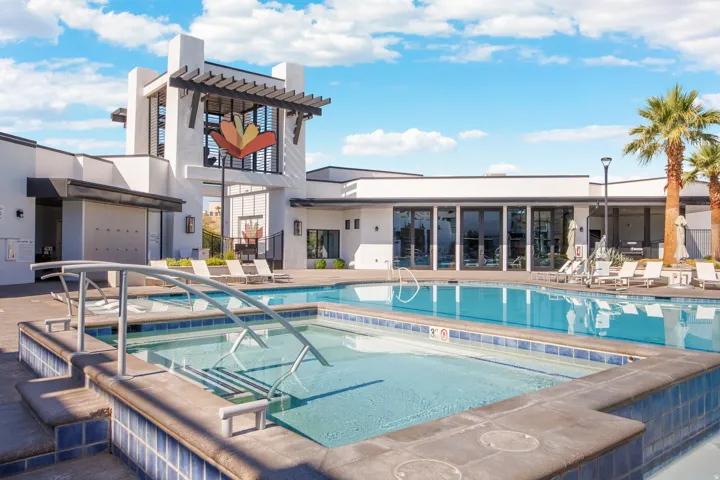 Expansive outdoor pool area featuring a large swimming pool, an integrated spa with handrails, and a modern building with a distinctive architectural facade