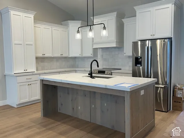 Kitchen featuring white shaker-style cabinetry, a contrasting wood-finish kitchen island with a light-toned countertop, a tile backsplash, stainless steel appliances, and wood-finish flooring