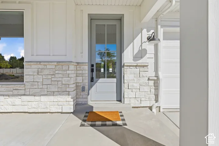 Entryway featuring a paneled door with glass inserts, stone veneer detailing, board and batten siding, an exterior wall sconce, and a concrete pathway