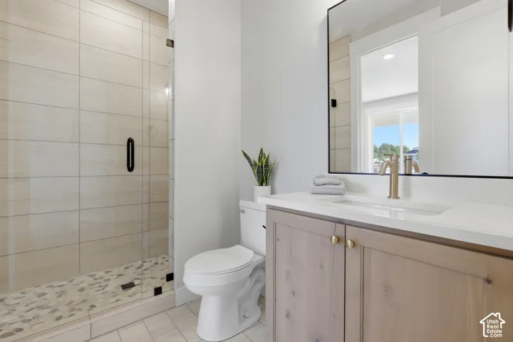 Modern primary bathroom featuring a spacious walk-in shower with subway tile surround and frameless glass enclosure, dual-sink vanity with wood-finish cabinetry and brushed brass hardware, quartz countertop, large framed mirror with integrated lighting, a
