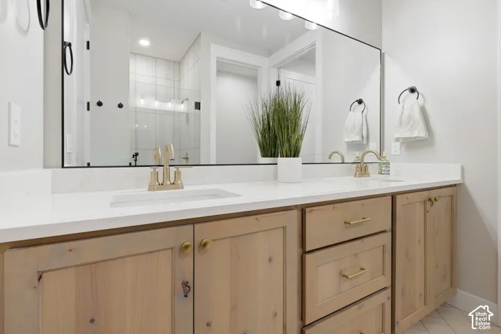 Dual under-mount sinks with brass-finish faucets, white stone countertops, natural wood cabinetry, and a large wall-mounted mirror