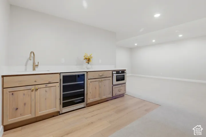 Light wood-finish cabinetry with gold-tone hardware, white countertop, integrated beverage refrigerator, built-in microwave, and recessed lighting