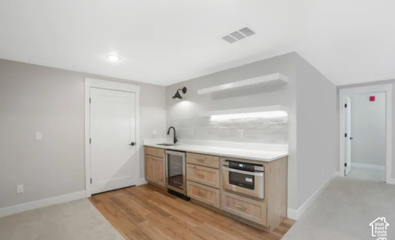 Built-in wet bar featuring wood cabinetry, white countertop, integrated beverage refrigerator, and stainless steel microwave