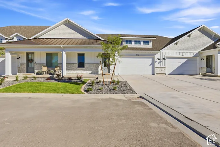 Contemporary exterior with white siding and gray stone accents, featuring a covered porch, a brown metal roof, and an attached two-car garage