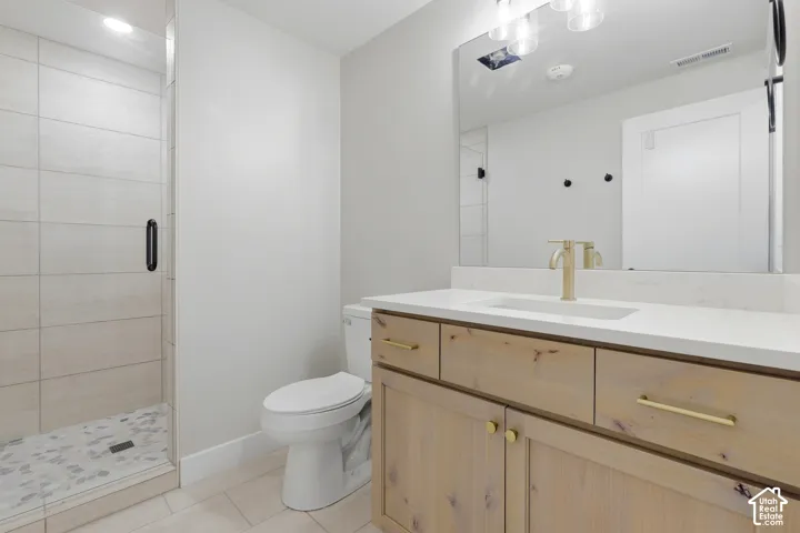 Walk-in shower with tiled walls and pebble floor, toilet, wood-finish vanity with gold-tone hardware, rectangular sink, and gold-tone faucet, large mirror, and overhead lighting