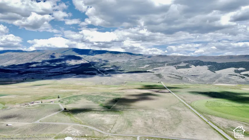 Expansive rural landscape with distant mountains, open fields, and a visible road