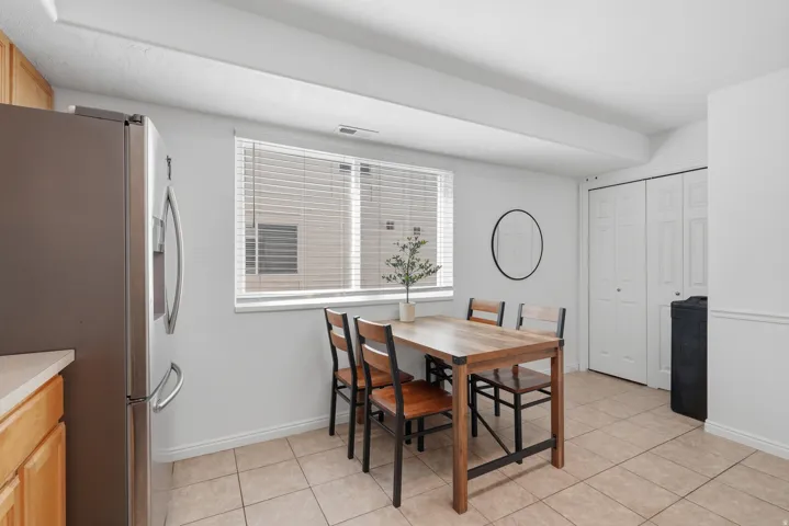 Stainless steel refrigerator, wood-finish cabinetry, tile flooring, window with blinds, bi-fold doors