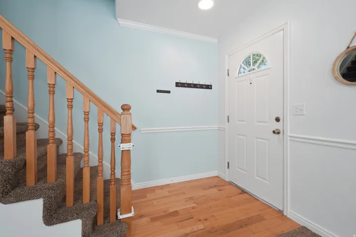 Wood-finish flooring with a white paneled entry door and a staircase featuring wood balusters