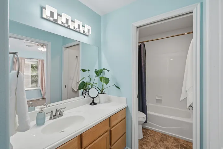 Bathroom featuring a single vanity with wood-finish cabinetry, a large mirror, a chrome faucet, a rectangular under-mount sink, and a shower-tub combination
