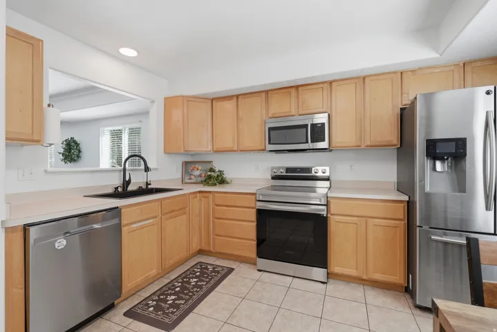 Kitchen featuring wood-finish cabinetry, stainless steel appliances, a black basin sink with a gooseneck faucet, and tiled flooring