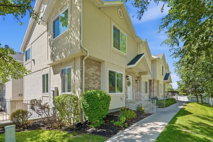 Tan stucco exterior with brick accents, white window trim, and a gabled roofline