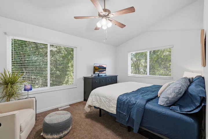 Vaulted ceiling with a ceiling fan, dual windows with blinds, and carpeted flooring