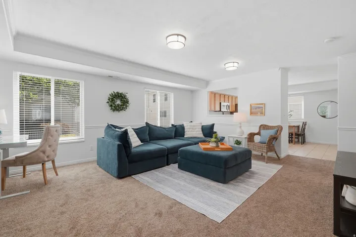 Recessed wall opening to kitchen, multiple windows, plush carpet flooring, integrated ceiling lighting, and crown molding