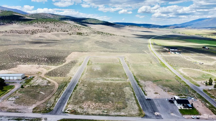 Expansive land parcel with paved access, mountainous terrain, and distant buildings