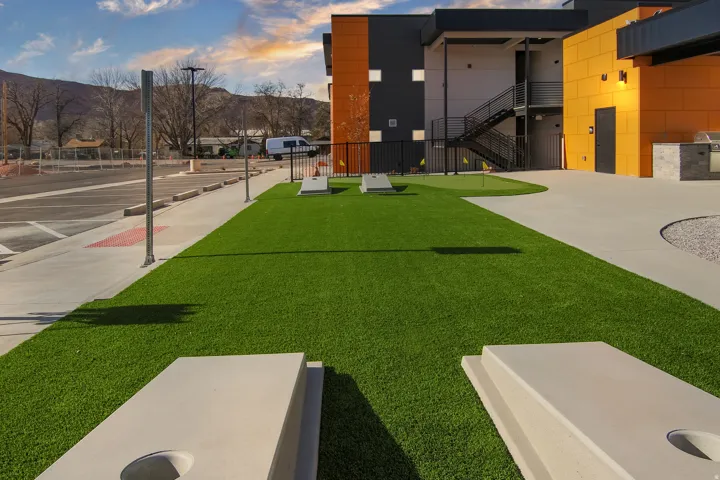 Artificial turf lawn, putting green, concrete walkways, outdoor grilling station, and exterior building with modern design elements