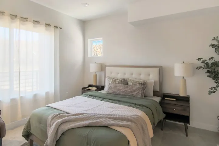 Recessed ceiling lighting, light-toned wall finishes, upholstered headboard, large window with sheer drapes, and a secondary high window