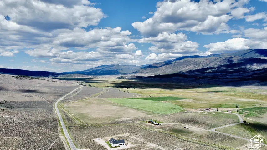 Expansive landscape featuring distant mountains, a roadway, and a mix of green and dry fields