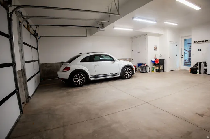 Spacious garage with a concrete floor, multiple fluorescent light fixtures, white walls, and a large overhead garage door