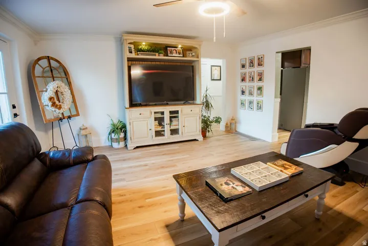 Recessed media console with integrated storage, ceiling fan light fixture, wood-finish flooring, and crown molding