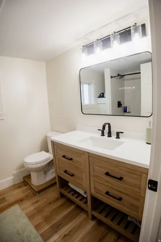 Wood-finish flooring, white walls, wood-finish vanity with drawer storage, white countertop with integrated sink, and a black framed mirror