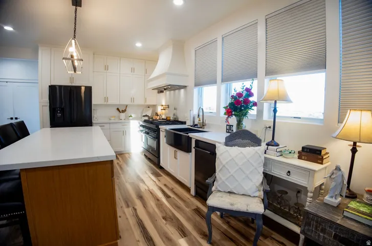 Kitchen featuring white cabinetry, a central island with a light-toned countertop, wood-finish flooring, a black appliance suite, and multiple windows with blinds